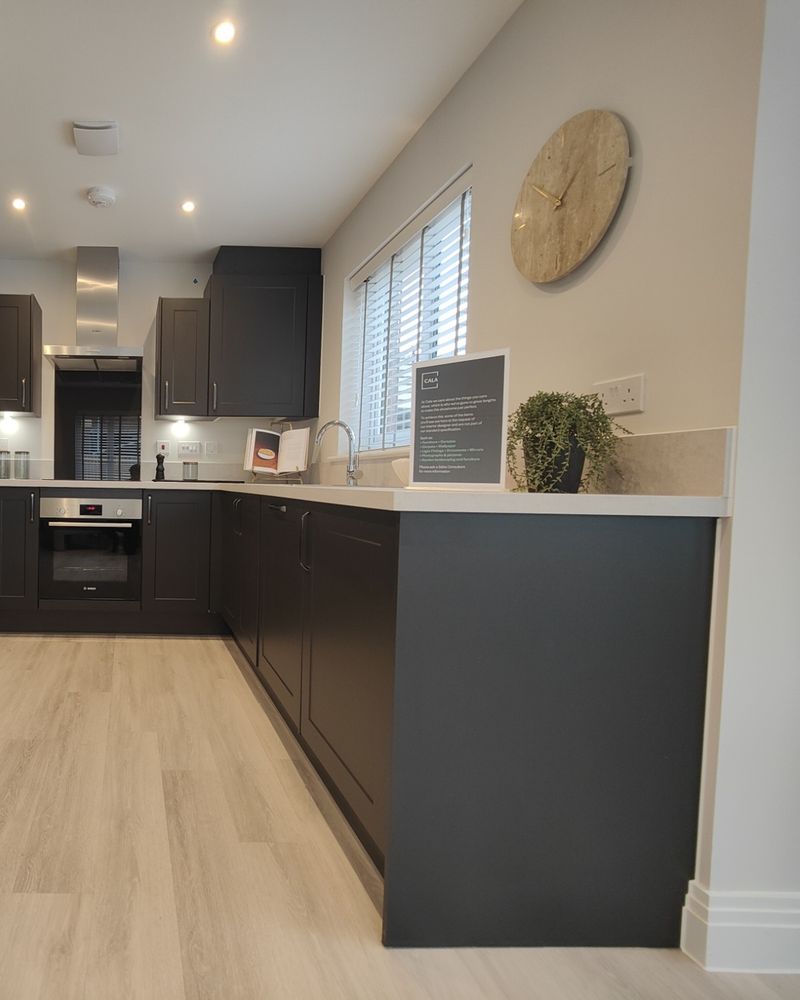 A dark fitted kitchen with a pale worktop, wood-toned floor and a window.