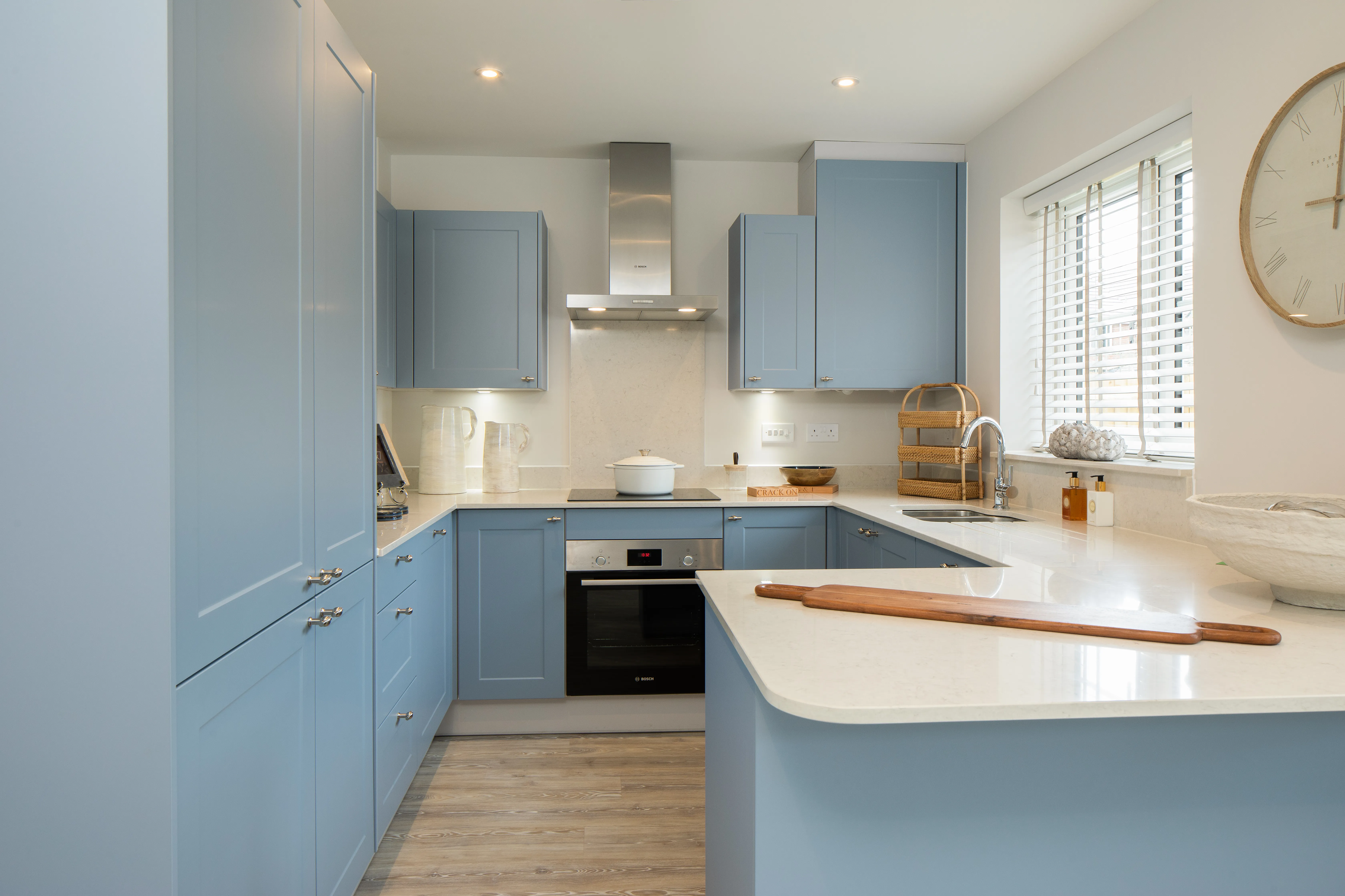 Blue fitted kitchen with white worktops and a large peninsula.