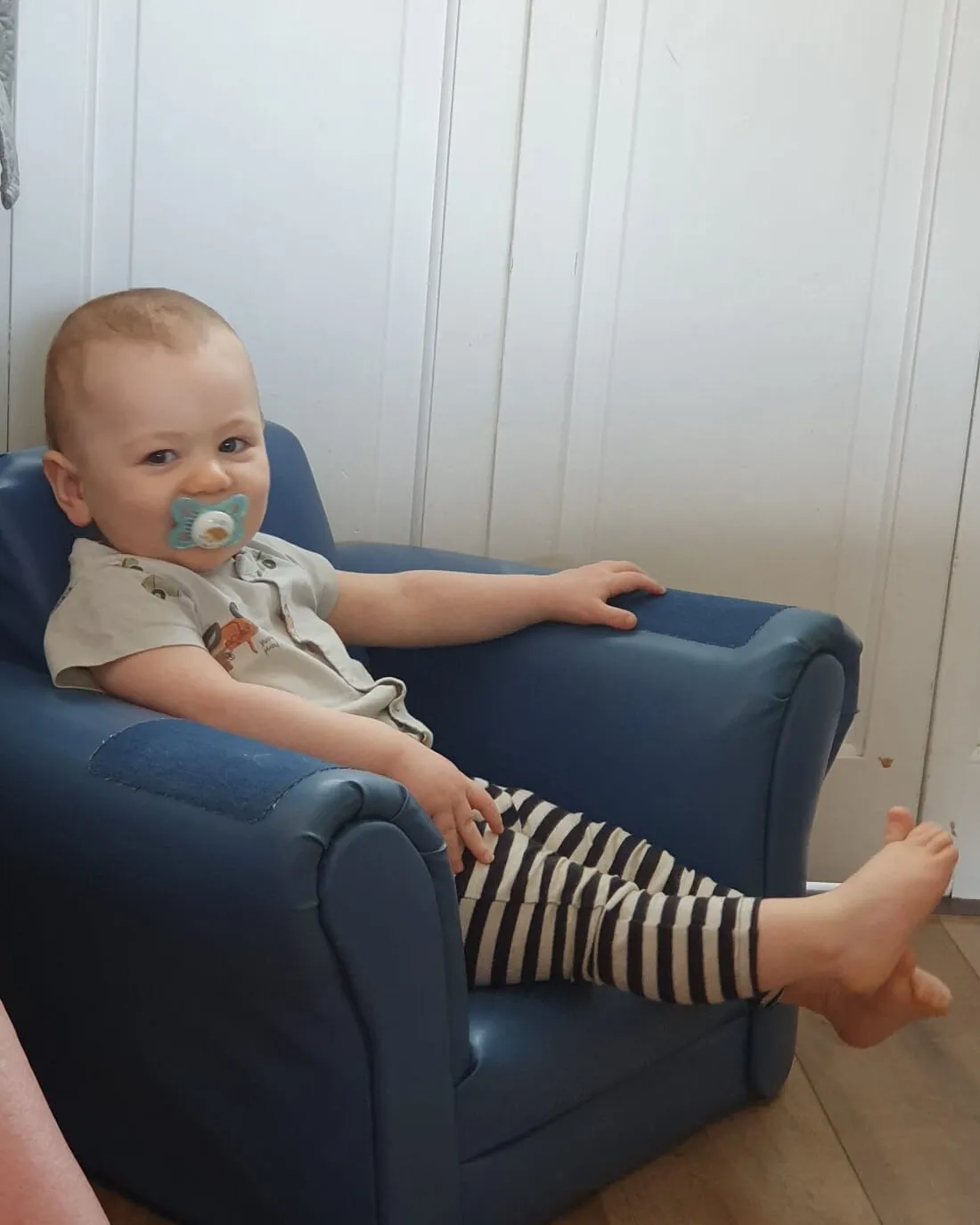 A young child sitting in a blue armchair at home.