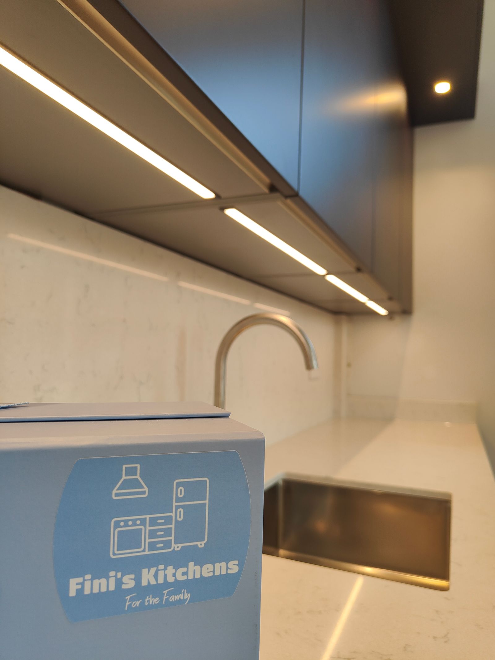 Fini’s Kitchens handover bag beside the sink, with white quartz surfaces and lighting beneath the wall cabinets.