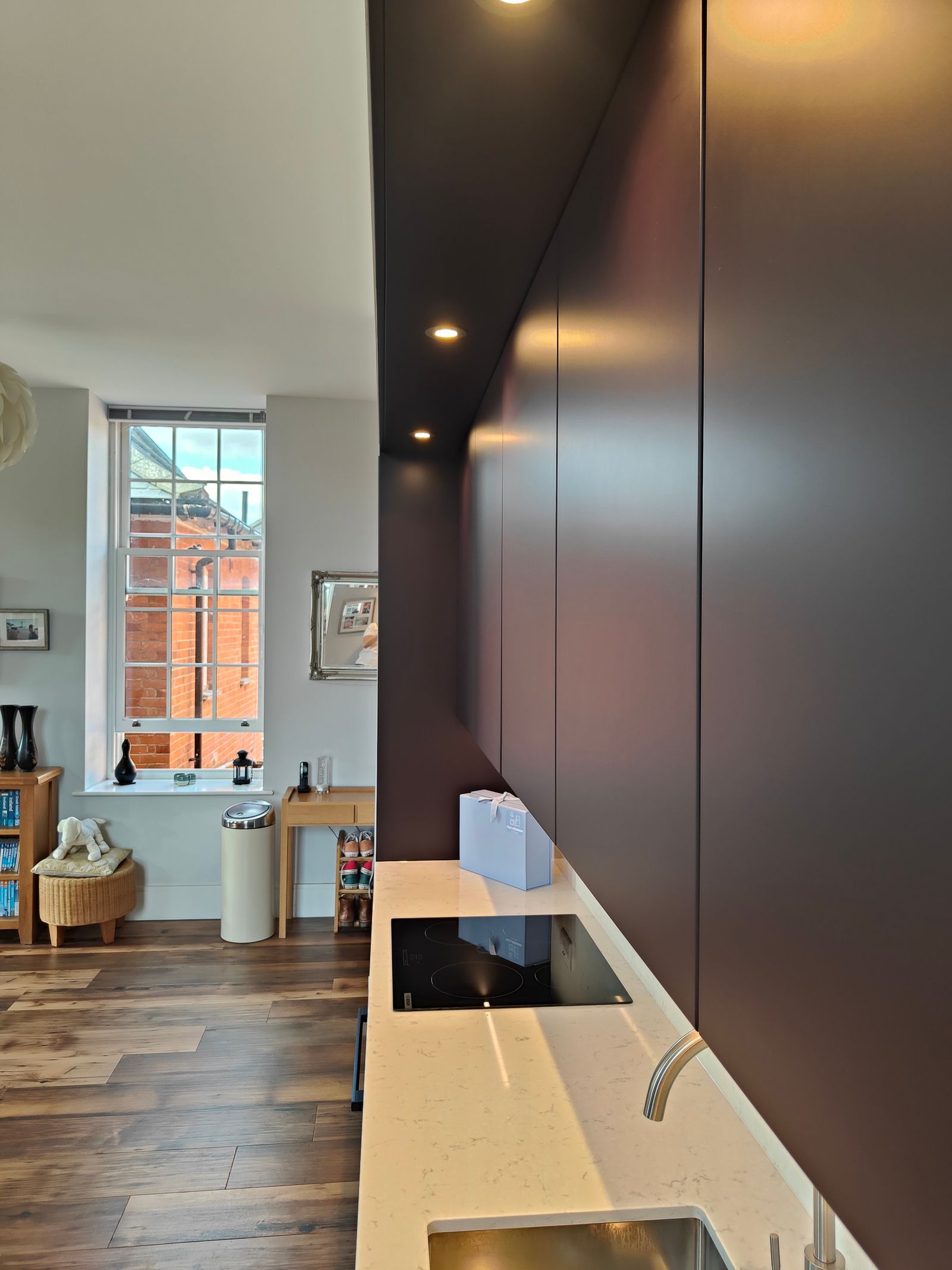 View along the white quartz worktop, with a sink in the foreground, hob and aubergine wall cabinets above.