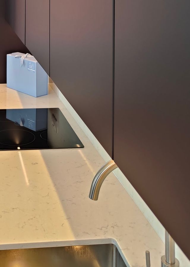A pale worktop and curved tap beneath dark cabinetry.